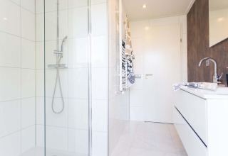 Baño moderno con ducha, azulejos blancos y lavabo en Collosseo Wellness de Résidence Valkenburg, Países Bajos.