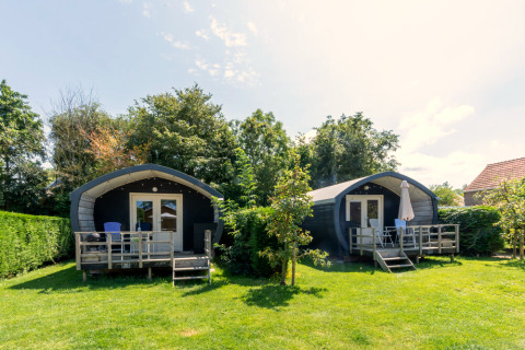 Twee gezellige Cocon-hutten met terrassen en tuinmeubilair, omringd door groen in het zonnetje.
