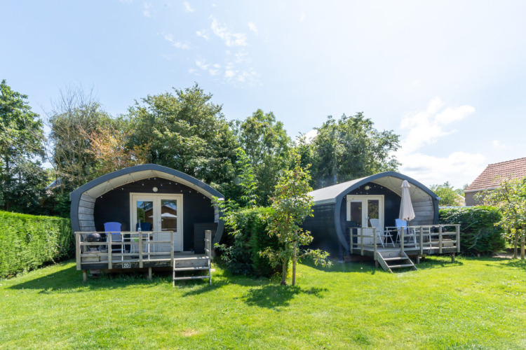 Two cozy Cocon cabins with small decks, garden seating, and greenery in a sunny countryside setting.