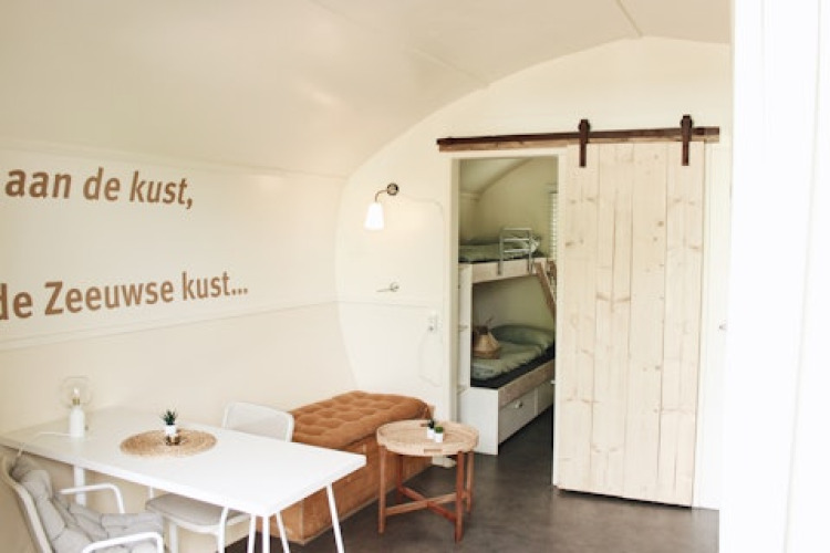 Bright, modern cabin interior with bunk beds, dining table, and wall text in Cocon at 7Huizen aan Zee, Netherlands.