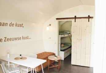 Interior luminoso y moderno de cabaña con literas, mesa de comedor y texto en la pared en Cocon, 7Huizen aan Zee.