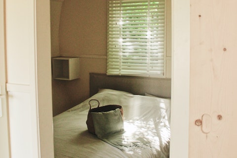 Uitzicht op een knusse slaapkamer in Cocon bij 7Huizen aan Zee, Nederland, met een tas op het bed.