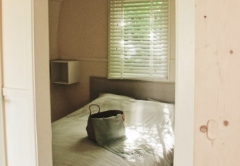 Vista su una camera accogliente nella cabina Cocon a 7Huizen aan Zee, Paesi Bassi, con borsa sul letto.