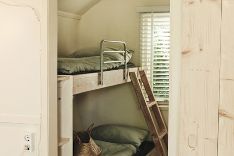 Houten stapelbed met groene dekens en een raam op de achtergrond in een gezellige hut bij Cocon, 7Huizen aan Zee.
