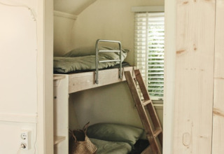 Litera de madera con sábanas verdes y una ventana de fondo en una cabaña acogedora de Cocon, 7Huizen aan Zee.