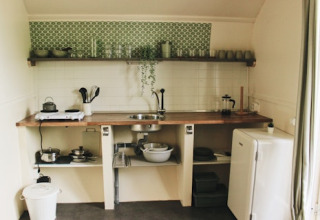 Rustieke keuken in een cabin met open planken, groene tegels, fornuis, servies en een kleine koelkast.