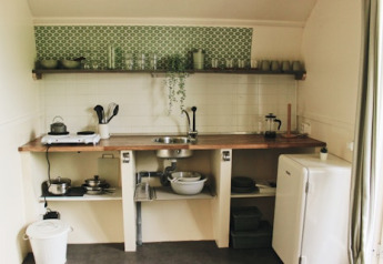 Cucina rustica in una cabina con scaffali aperti, piastrelle verdi, stoviglie e un piccolo frigorifero.