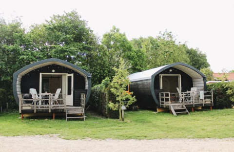 Dos acogedoras cabañas Cocon con porches en 7Huizen aan Zee, rodeadas de árboles verdes en los Países Bajos.