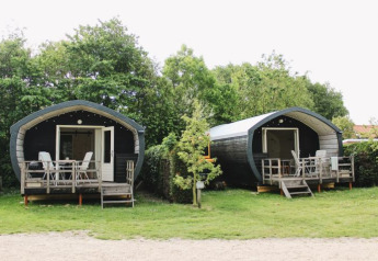 Dos acogedoras cabañas Cocon con porches en 7Huizen aan Zee, rodeadas de árboles verdes en los Países Bajos.