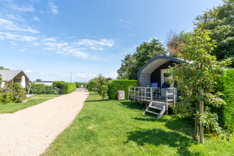 Alojamiento glamping con cabañas y tiendas junto a un sendero de grava, rodeado de naturaleza verde.