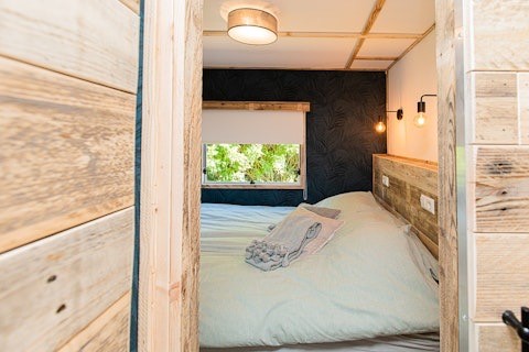 Cozy lodge bedroom with wooden walls, double bed, window view and soft lighting, photographed from door.