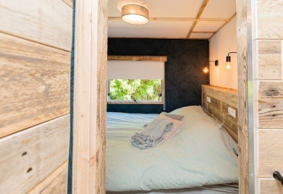 Cozy lodge bedroom with wooden walls, double bed, window view and soft lighting, photographed from door.
