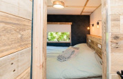 Knusse lodge slaapkamer met houten wanden, dubbel bed en raam, gefotografeerd van aan de deur.