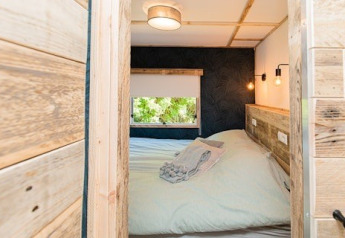 Chambre de lodge chaleureuse avec murs en bois, lit double, fenêtre et éclairage doux, vue depuis la porte.