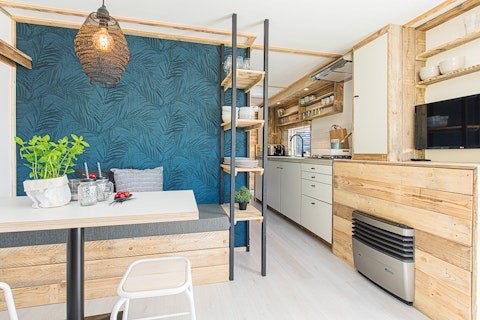 Cocina y comedor de una cabaña moderna, con toques de madera, pared azul y estanterías abiertas.