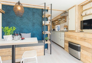 Cocina y comedor de una cabaña moderna, con toques de madera, pared azul y estanterías abiertas.