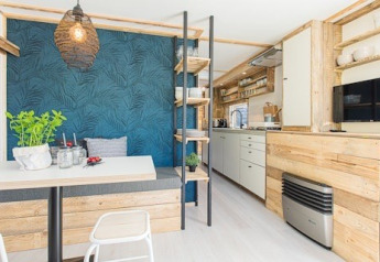 Cucina e zona pranzo di un lodge moderno, legno chiaro, parete blu e dettagli di design e piante.