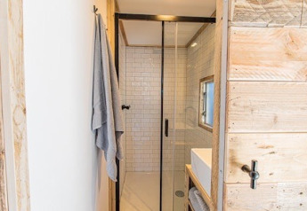 Modernes Badezimmer in einer Lodge mit Glasdusche, weißen Fliesen, Handtuch und Holzwänden.
