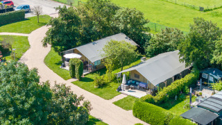 Aerial view of safari tents on a green campsite with pathways, hedges, and parked cars in the background