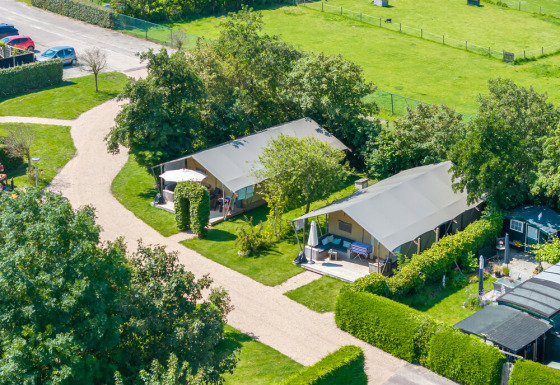 Luchtfoto van safaritenten op een groene camping met wandelpaden, hagen en geparkeerde auto's in de verte