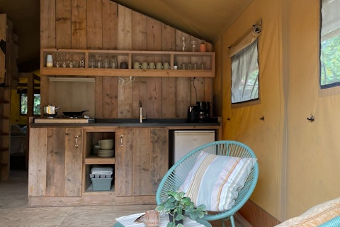 Interior de una tienda safari con cocina de madera, silla azul y ventanas en 7Huizen aan Zee, Países Bajos.