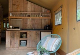 Interno di tenda safari con cucina in legno, sedia azzurra e finestre a 7Huizen aan Zee, Paesi Bassi.