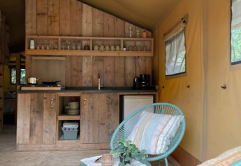 Intérieur d’une tente safari avec cuisine bois, chaise bleue et fenêtres à 7Huizen aan Zee, Pays-Bas.