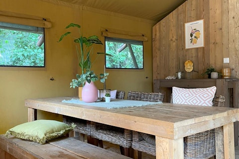 Interieur van een safaritent met houten tafel, rieten stoelen en planten bij 7Huizen aan Zee in Nederland.