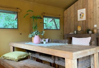 Interieur van een safaritent met houten tafel, rieten stoelen en planten bij 7Huizen aan Zee in Nederland.