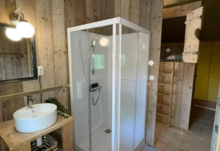 Baño dentro de la tienda safarí en 7Huizen aan Zee, Países Bajos, con ducha, lavabo y espejo visible.