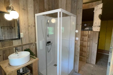 Badezimmer im Safari-Zelt bei 7Huizen aan Zee in den Niederlanden mit Dusche, Waschbecken und Spiegel.
