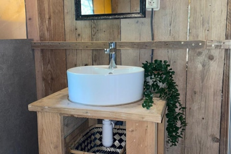 Salle de bain rustique avec murs en bois, vasque ronde et miroir dans une tente safari à 7Huizen aan Zee.
