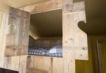 Innenansicht eines Safarizeltes mit Holzbett und kariertem Bettbezug bei 7Huizen aan Zee, Niederlande.