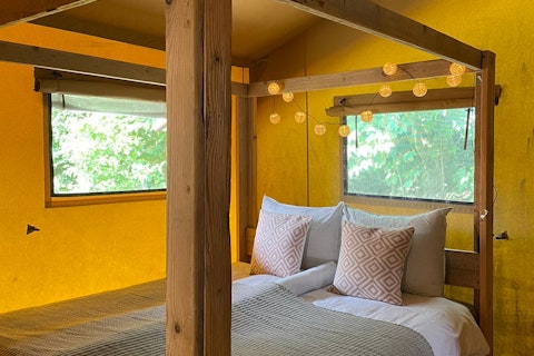 Interior de tienda safari con paredes amarillas, cama con dosel y luces en 7Huizen aan Zee, Países Bajos.