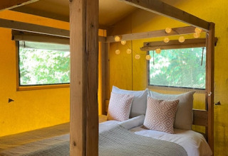 Interior de tienda safari con paredes amarillas, cama con dosel y luces en 7Huizen aan Zee, Países Bajos.