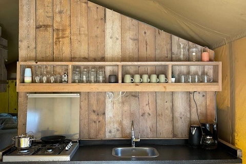 Rustikale Küche im Safarizelt bei 7Huizen aan Zee, Niederlande, mit Holzwand und offenen Regalen.