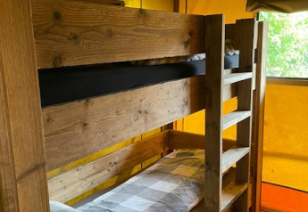 Køjeseng i træ indenfor en safaritelte ved 7Huizen aan Zee, oplyst af naturligt lys gennem gule sider.