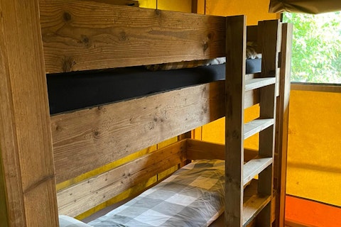 Holzetagenbett im Inneren eines Safarizelts bei 7Huizen aan Zee, mit warmem Licht und Fensteransicht.