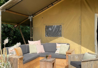 Udendørs siddeområde ved en safaritelt med grå sofaer og puder på 7Huizen aan Zee i Nederlandene.