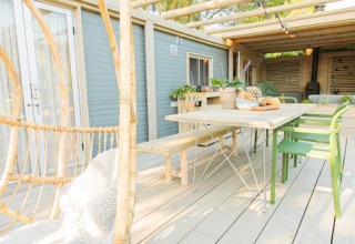 Buitenterras van Lodge 2 en 3 bij 7Huizen aan Zee in Nederland, met houten tafel, bankje en groene stoelen.