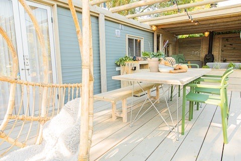 Buitenterras van Lodge 2 en 3 bij 7Huizen aan Zee in Nederland, met houten tafel, bankje en groene stoelen.