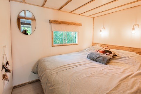 Dormitorio con cama grande, espejo redondo y ventana, Lodge 2 y 3, 7Huizen aan Zee en los Países Bajos.