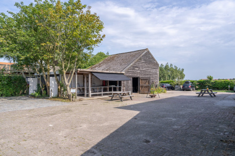 Vista exterior de Lodge 2 y 3 en 7Huizen aan Zee, Países Bajos, con granero de madera, mesas y autos estacionados.