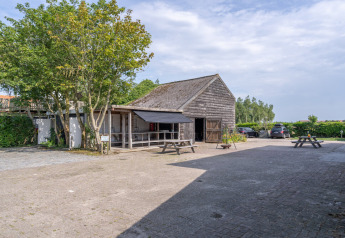 Vista esterna delle Lodge 2 e 3 presso 7Huizen aan Zee nei Paesi Bassi, con fienile in legno, tavoli e auto.