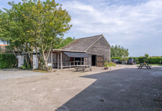 Vista exterior de Lodge 2 y 3 en 7Huizen aan Zee, Países Bajos, con granero de madera, mesas y autos estacionados.