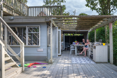 Holzterrasse einer Lodge bei 7Huizen aan Zee mit zwei Personen, die Essen und Getränke genießen.