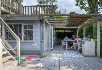 Udendørs træterrasse ved Lodge 2 og 3 på 7Huizen aan Zee med to personer, der nyder mad og drikke.