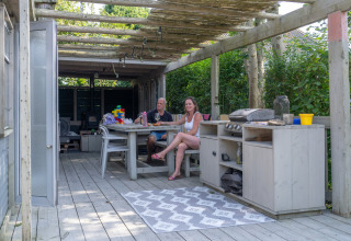 Udendørs terrasse ved Lodge 2 og 3 på 7Huizen aan Zee i Holland med to personer, bord og grillkøkken.
