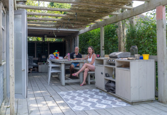 Udendørs terrasse ved Lodge 2 og 3 på 7Huizen aan Zee i Holland med to personer, bord og grillkøkken.