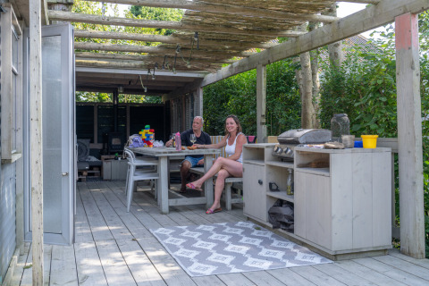 Covered wooden terrace at Lodge 2 and 3 at 7Huizen aan Zee in the Netherlands, with two people dining.